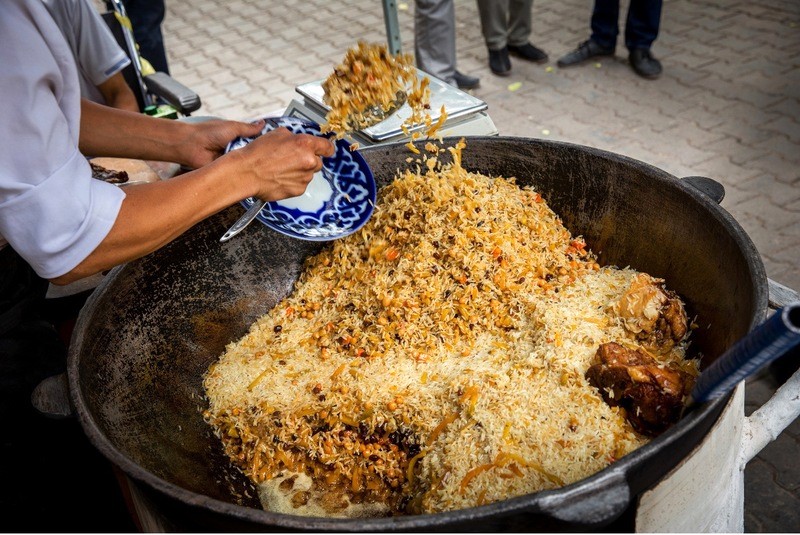 Oshpaz, đầu bếp plov, trình bày món plov nóng hổi trên đĩa xanh truyền thống, họa tiết phương Đông. (Ảnh: changeinuzbekistan)